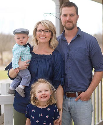 adoptive family of 4 poses together outside on the porch and smiles at the camera while talking to kids about siblings