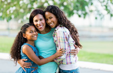 two teens in open adoption hug their adoptive mom outside