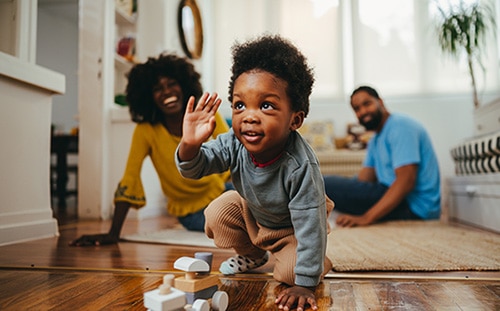 African American toddler playing with a wooden train toy at home while his adoptive parents smile